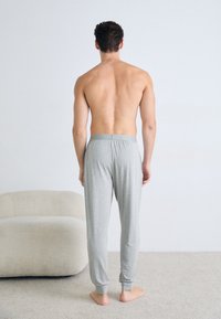 Pantaloni de pijama gri din bumbac, cu un elastic la talie, manșete înguste și un branding subtil pe talie, văzuți din spate.