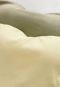 Coussins en tissu doux vert olive et jaune pâle avec une fine texture côtelée disposés côte à côte.