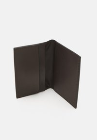 Brun lærveske med en glatt tekstur, som har innvendige lommer og et minimalistisk design; ingen synlig maskinvare eller mønstre.