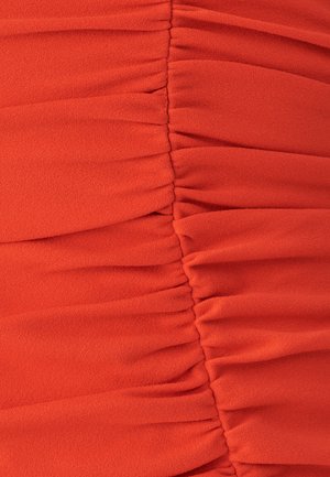Zahnědlá oranžová tkanina s jemnou texturou, která má nerovnoměrné skladby uspořádané vodorovně, čímž vytváří prostorově texturovaný povrch.