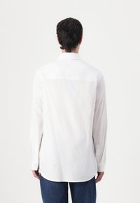 White long-sleeve shirt with a straight-cut hem, button cuffs, and subtle texture. Back view shows a classic collar and smooth fabric.