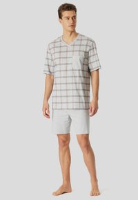 Man standing barefoot wearing a short-sleeve gray plaid V-neck shirt with chest pocket and solid gray shorts against a plain background.