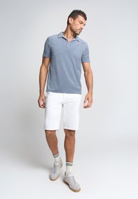 Lichtblauwe polo met korte mouwen en kraag, gecombineerd met witte shorts en lichtgrijze sneakers met donkere accenten.