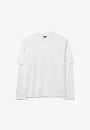 Chemise à manches longues à superposition de manches courtes, de couleur blanche, à col rond, avec une broderie discrète de la marque près du poignet gauche.