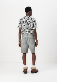 Kortærmet sort-hvid blomster skjorte, grå denim shorts og brune støvler med en fluffy tan krave, set fra ryggen.