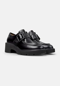 Black leather shoes with a rounded toe, featuring a prominent buckle strap and a chunky black platform sole with textured tread.