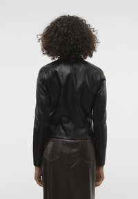 Zwarte leren jas met een getailleerd ontwerp, gladde textuur en opvallende stikdetails, gecombineerd met een bruine leren rok.