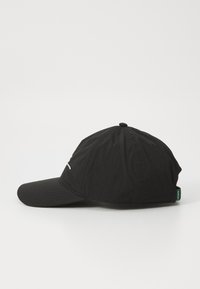 Fekete baseball sapka ívelt napellenzővel, szövettextúrával és egy kis zöld címkével az oldalon. Egyszerű dizájn varrással kiemelve.