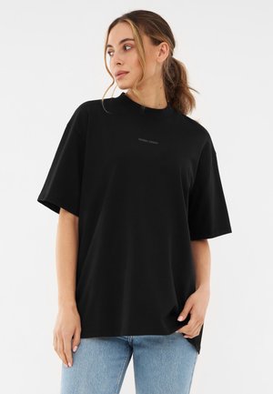 T-shirt noir surdimensionné en coton doux, avec un col rond, des manches courtes et un logo subtil imprimé sur le devant.