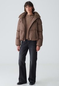 Brown puffer jacket with a textured fur collar, cropped design, and elastic cuffs paired with high-waisted dark jeans and black boots.