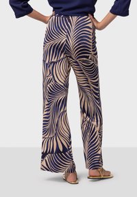 Pantalons larges présentant un motif de feuilles de palmier bleu marine et beige. Fabriqués dans un tissu doux avec une texture lisse et une taille élastique.