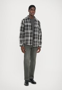 Svart- og hvit rutete flanellskjorte med knappestolpe i front, to brystlommer,parret med mørkegrønne jeans og svarte sko.