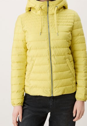 Veste matelassée jaune zippée avec capuche et cordons, portée sur un pantalon noir, montrée des épaules aux hanches.