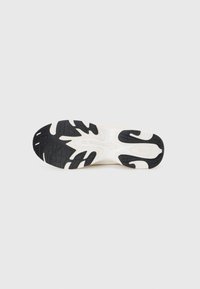 White and black rubber sneaker sole with a textured grip pattern and cut-out design elements. Features pronounced heel and arch support.