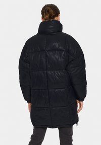 Svart puffjacka med hög krage, kviltat mönster och elastiska manschetter. Slät textur med dragsnörning i nederkant.