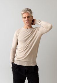 Beżowy sweter z długim rękawem, okrągłym dekoltem, gładką fakturą i dopasowanymi mankietami, w połączeniu z czarnymi spodniami.