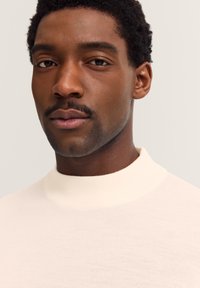 Cremefarbenen, hochgeschnittenen Pullover mit glatter Textur, taillierter Passform und dezenten Rippendetails am Kragen.