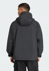 Mørkegrå vandtæt jakke med hætte, der har en løs pasform, elastiske manchetter og en glat tekstur. Minimalistisk design, ingen synlige logoer.