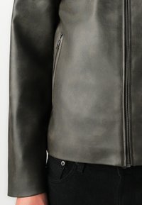 Close-up of a dark gray leather jacket with a front zipper and zippered side pocket, worn with black pants.