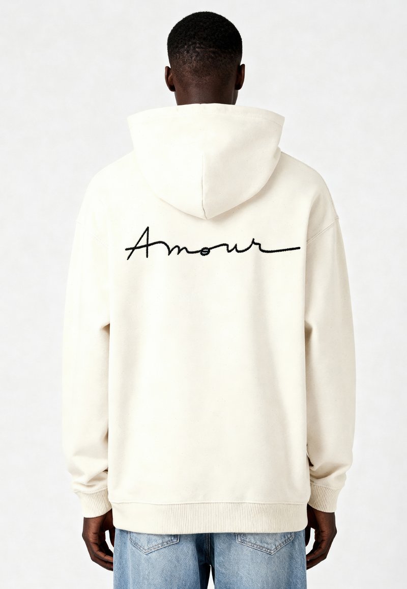 Felpa color crema con cappuccio regolabile. Presenta la scritta nera ricamata "Amour" sul retro. Polsini e orlo a coste. Design casual.