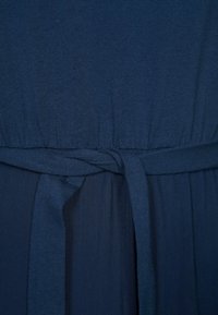 Tissu de robe bleu marine avec une texture côtelée, présentant une taille élastique et une ceinture nouée pour une définition supplémentaire à la taille.