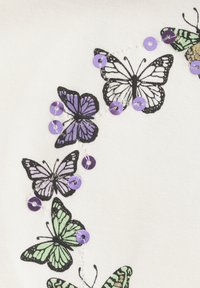 Weißer Stoff mit mehreren Schmetterlingsmotiven in Schwarz, Lila und Grün, akzentuiert mit lila Pailletten und weißen Fäden.