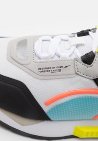 Vit och grå sneaker med en texturerad överdel, svart sula, turkosa accenter och orange detaljer; inkluderar ett märkesetikett på tungan.