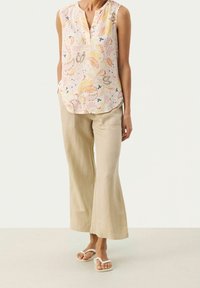 Blouse sans manches à motifs floraux dans des tons pastel, avec un col à patte de boutonnage. Associée à un pantalon large en lin beige et des sandales blanches.