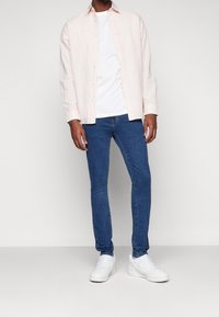 Světle růžová košile na knoflíky přes bílém tričku, v kombinaci s úzkými modrými džíny a bílými teniskami. Hladká látka a volný styl.