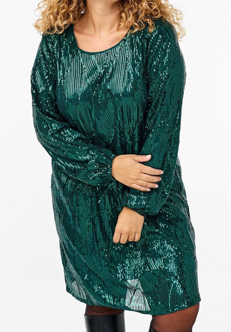 Grön paljettklänning med rundad halsringning, långa ärmar och lös passform, med en texturerad yta och glittrande detaljer genom hela.