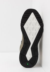 Suela de zapato Timberland que presenta goma negra y una entresuela blanca texturizada con patrón de diamante y un acento verde. Diseñada para ofrecer tracción y durabilidad.