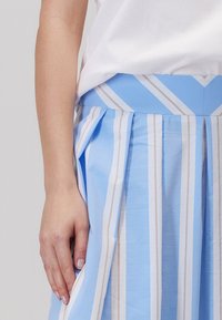 Jasnoniebieska spódnica plisowana z pionowymi białymi i beżowymi paskami, z dopasowanym pasem i widocznymi bocznymi kieszeniami.