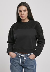 Felpa nera con pannello in pizzo testurizzato sulle spalle e corpo liscio. Design cropped, polsini e orlo a coste. Abbinata a jeans strappati.