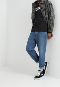 Sudadera negra con el logo blanco de "Levi's", camisa de botones gris con estampado, jeans de mezclilla azul y zapatillas de caña alta negras con acentos blancos.
