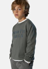 Grauer Sweatshirt mit "NORTH SAILS" in Blau gestickt. Mit Rundhalsausschnitt und gerippten Bündchen, getragen über einem weißen Hemd.