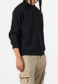 Černá mikina s kulatým výstřihem, dlouhými rukávy a žebrovanými manžetami. Hladká textura, s minimalistickým designem a bez viditelných log.