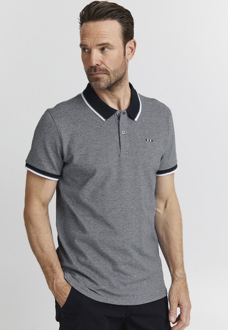 Pilkos spalvos polo marškiniai su juodu apykaklė ir baltais akcentais, turintys dviejų mygtukų uždarymą ir nedidelį logotipą krūtinėje. Lygus audinio paviršius.