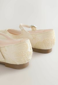 Beige Mary-Jane-Schuhe aus Stoff mit bestickten Muschelmustern, abgerundeten Zehen und kleinem Absatz. Verfügt über einen verstellbaren Knöchelriemen mit silberner Schnalle.