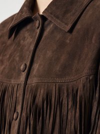 Veste en daim marron avec des franges le long de l'ourlet et des épaules, dotée d'un col classique et d'une fermeture à boutons. Texture douce.