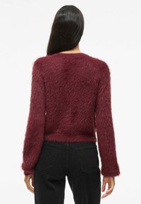 Pull en velours bordeaux à surface texturée, col rond et manches longues, associé à un jean noir taille haute.