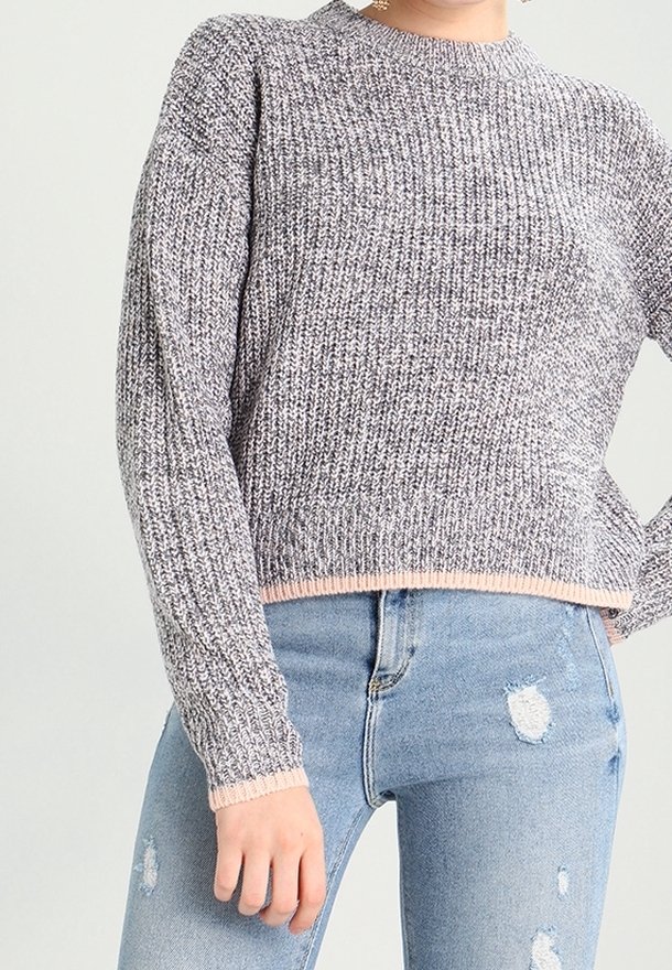 Szary sweter dzianinowy z teksturowanym wzorem i różową lamówką. Bezkołnierzykowy krój z długimi rękawami, zestawiony z podartymi, jasnoniebieskimi dżinsami.