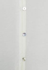 Vit skjorta med knappar av en slät textur, med fyra runda, pärlliknande knappar längs den centrala knäppningen.