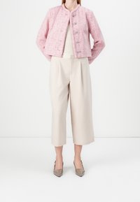 Růžový tweedový kabátek s kulatým výstřihem a pěti stříbrnými knoflíky, společně s béžovými širokými kalhotami a béžovými botami na podpatku s špičatou špičkou.