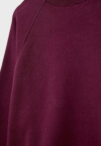 Bordo dukserica s teksturiranim materijalom, okruglim izrezom i raglan rukavima. Glatka površina bez vidljivih uzoraka ili dodataka.