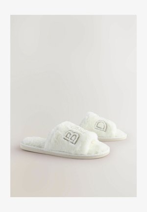 Pantofole bianche in peluche con una texture morbida, dotate di accenti di strass sulle cinghie e un design della suola soffice e imbottito.