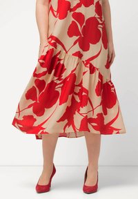Květinové midi šaty s červeným květinovým vzorem na béžovém pozadí, se stupňovitým lemem a bočními kapsami, doplněné červenými semišovými podpatky.