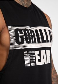 Zwarte mouwloze tanktop met opvallende witte tekst "GORILLA WEAR," voorzien van een gestructureerd grafisch ontwerp en ruwe armsgaten.