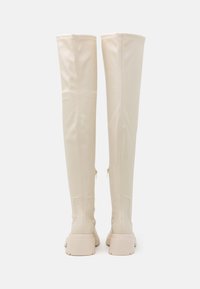 Knee-high beige boots made of smooth material, featuring a flat sole, side zippers, and stitching details along the seams.
