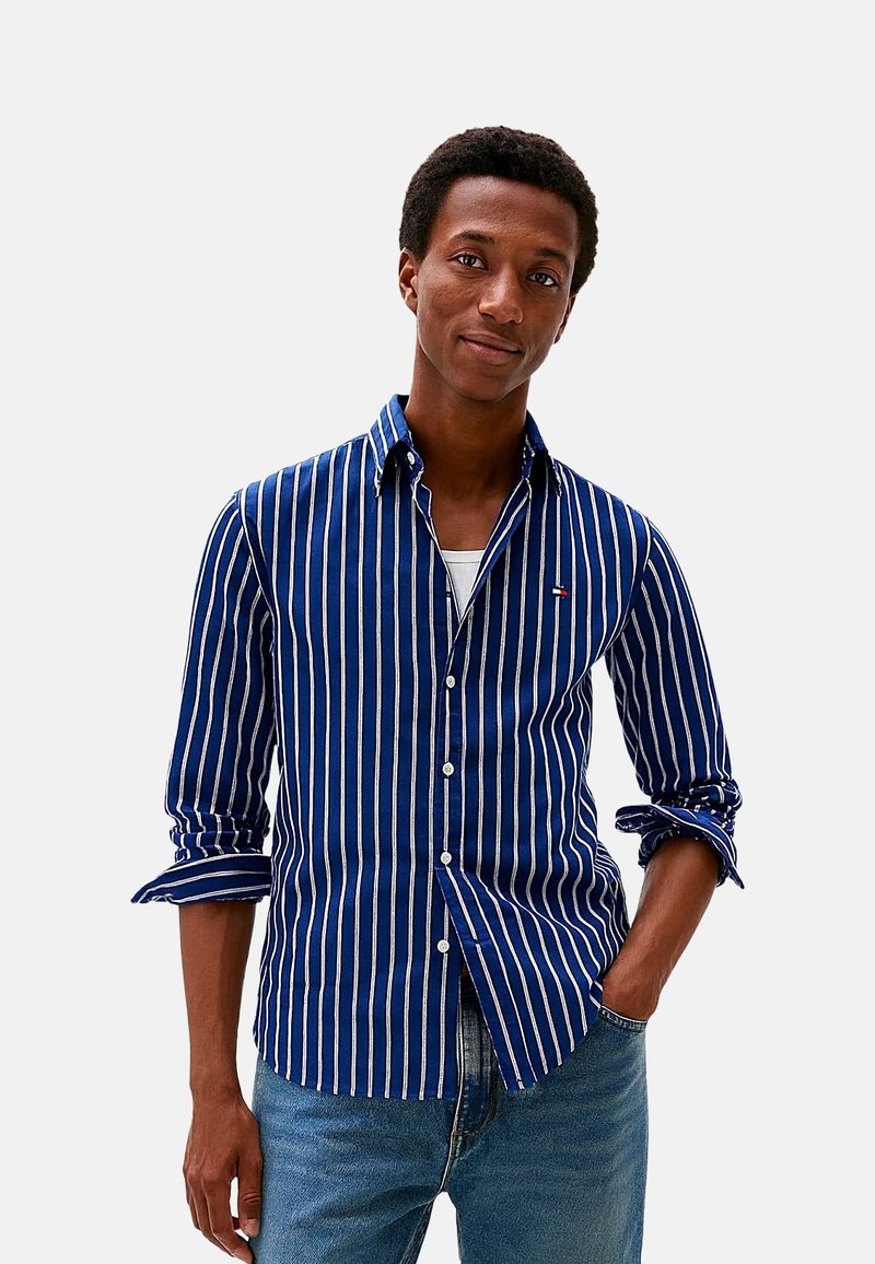 Camisa de botones con rayas azul marino y blancas, fabricada en tejido ligero, con un bolsillo y las mangas remangadas, combinada con unos vaqueros azul claro.