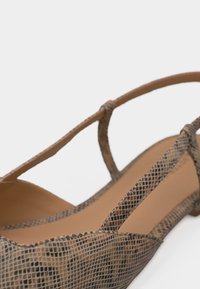 Καφέ επίπεδη σαγιονάρα με λεπτά λουράκια με σχέδιο φίδι και μυτερή μύτη, γυρισμένη πλάγια για να φαίνεται η πλευρά και η εσωτερική σόλα.